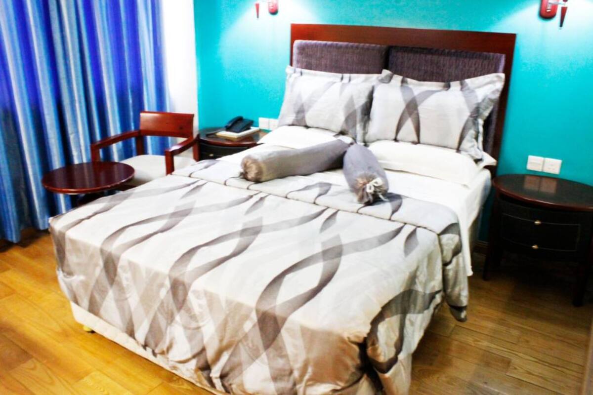A hotel room with a bed, a chair, a bedside table, and a curtain.
