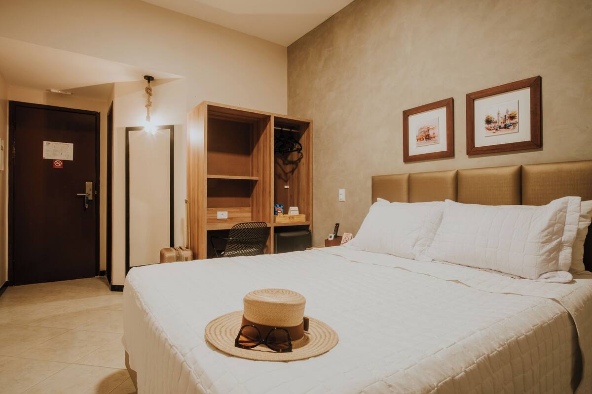 Una habitación de hotel con cama, armario, escritorio y dos cuadros en la pared.