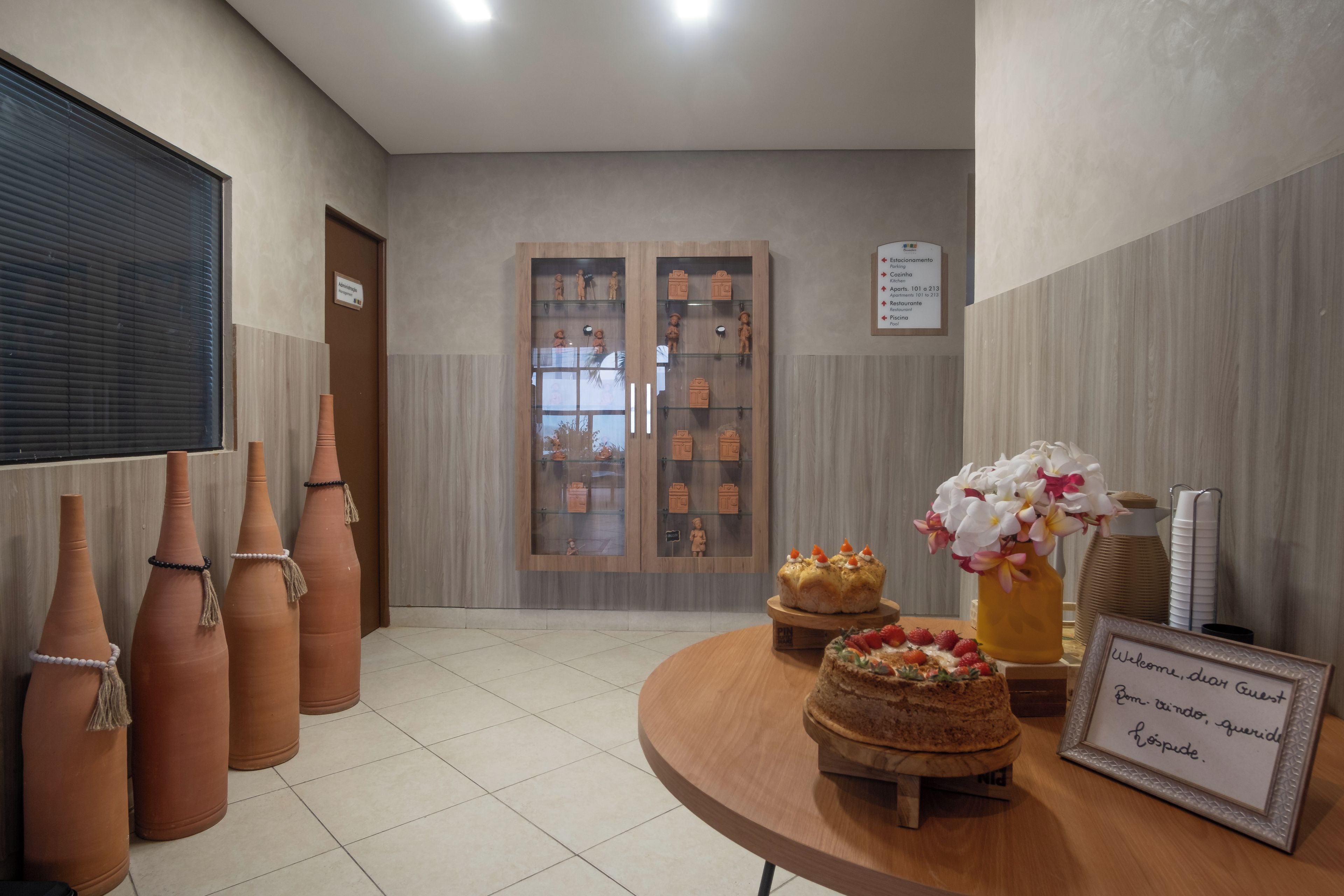 Un espace d’accueil d’hôtel avec un comptoir de réception en bois, des vases en terre cuite et un panneau d’accueil.