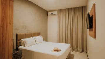 Habitación de hotel con cama, armario de madera, unidad de aire acondicionado, televisor montado en la pared y ventana con cortinas.
