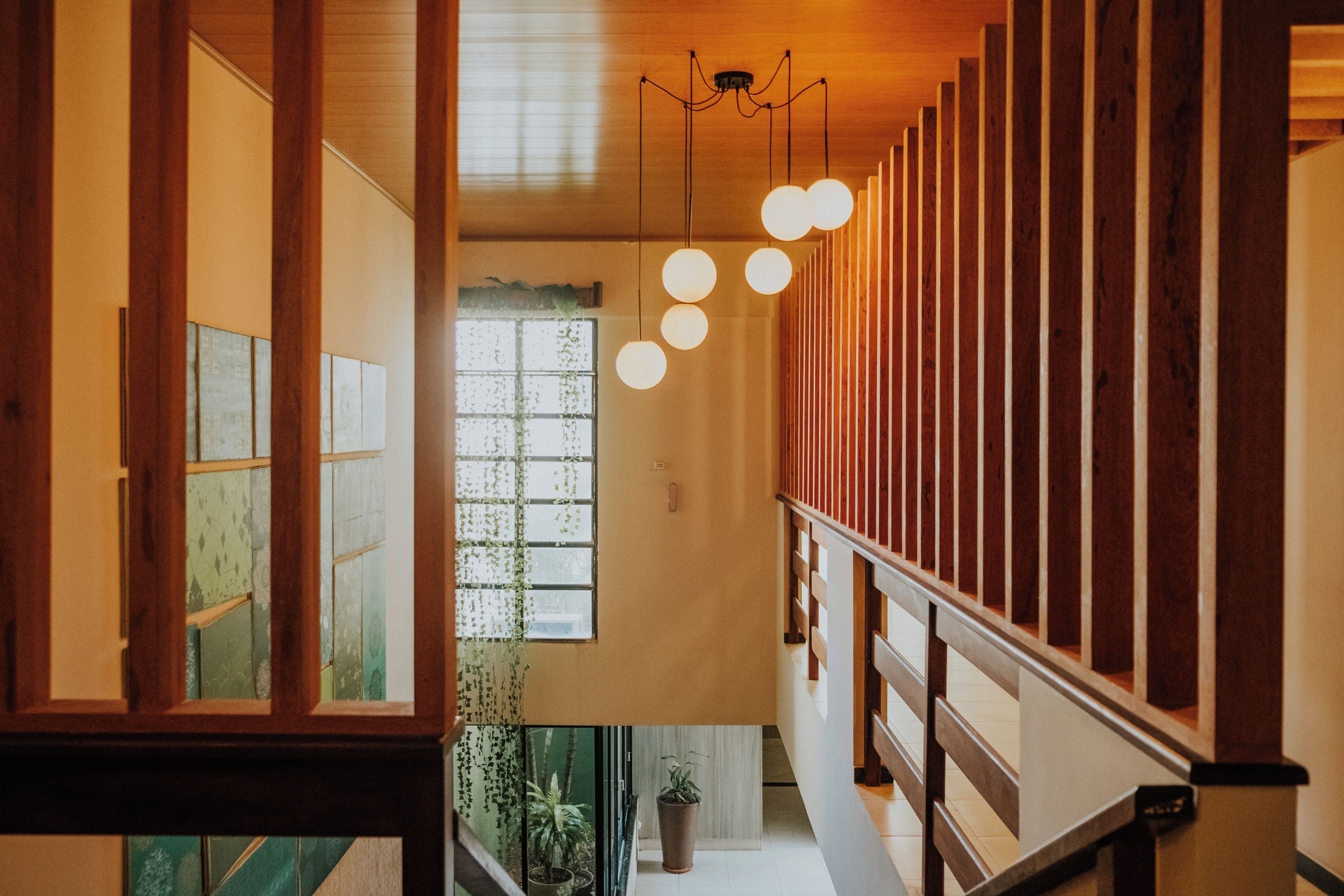 Una escalera de madera con barandilla, una lámpara colgante y un ventanal con vistas a follaje.