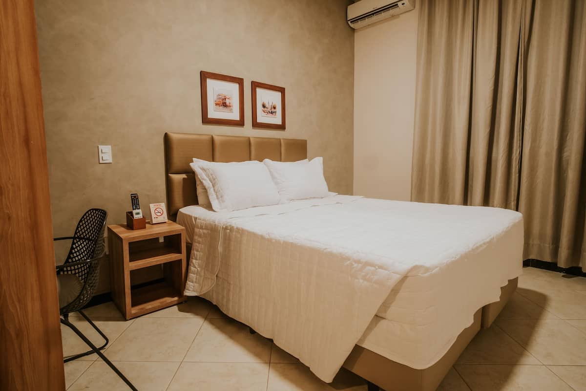 Habitación de hotel con cama, mesita de noche, una silla y dos cuadros en la pared.