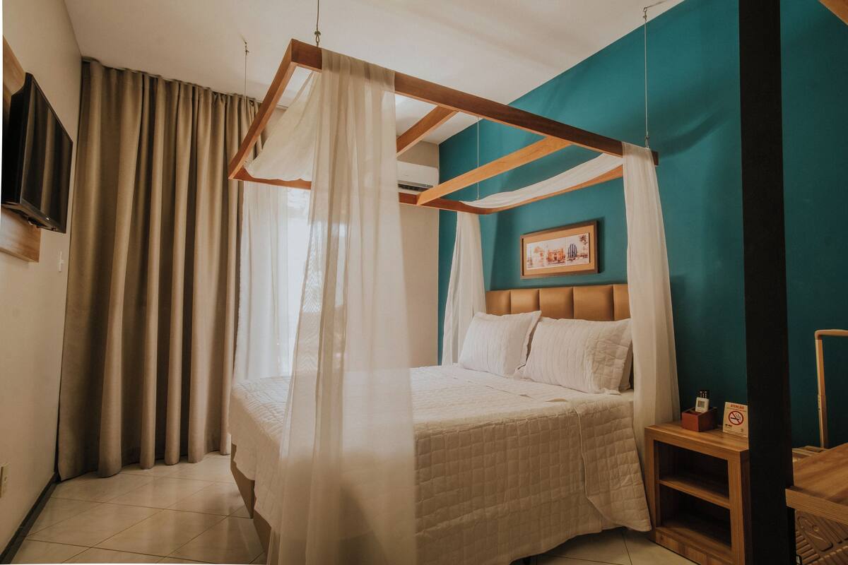Un dormitorio con cama bajo dosel, una mesita de noche con reloj y televisor montado en la pared.