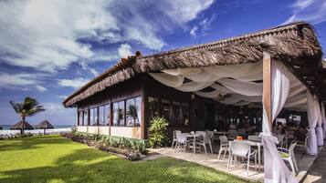 A restaurant with a thatched roof, outdoor seating, and a view of the ocean.