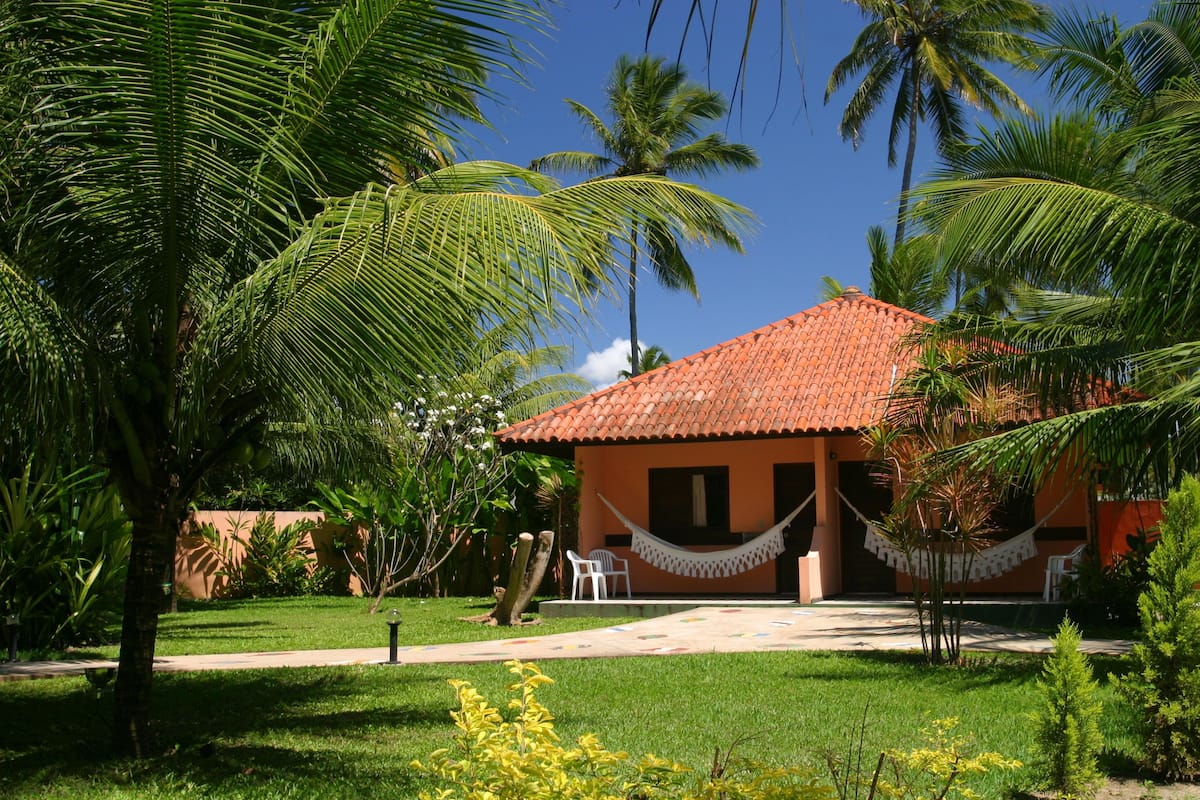 Una casa con techo de tejas rojas, rodeada de abundante vegetación y palmeras.