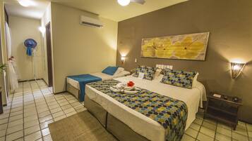 Een hotelkamer met een groot bed, een klein bureau, een stoel, een ventilator, een airconditioner aan de muur en een schilderij.