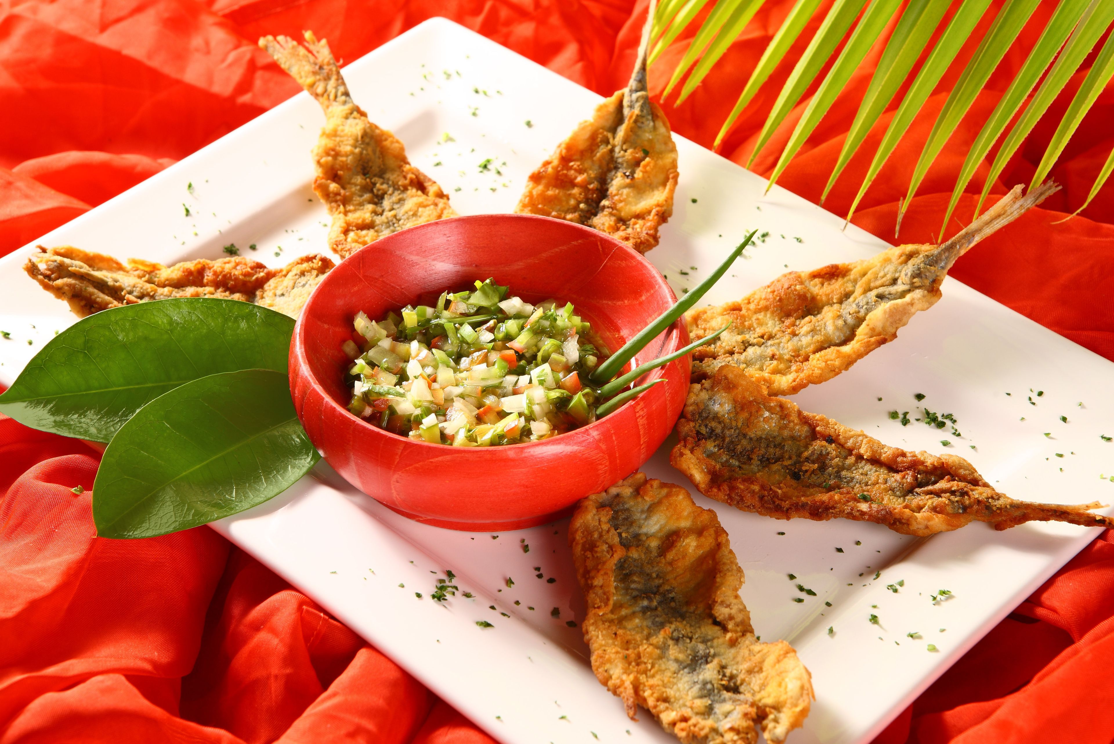 A plate of fried fish with a side of chopped vegetables and herbs.