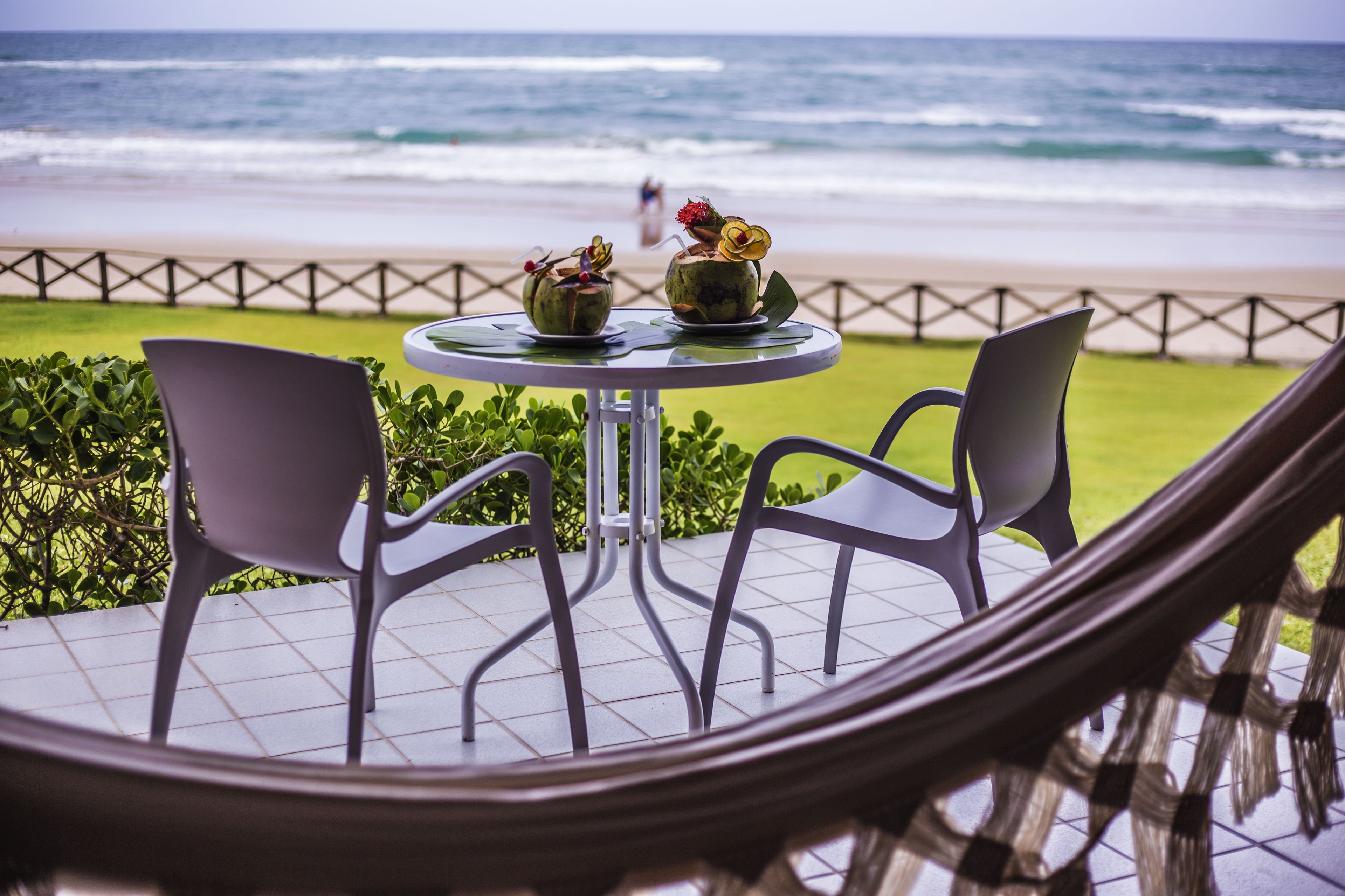 A round table with two chairs and two decorative vases on a balcony overlooking the beach.