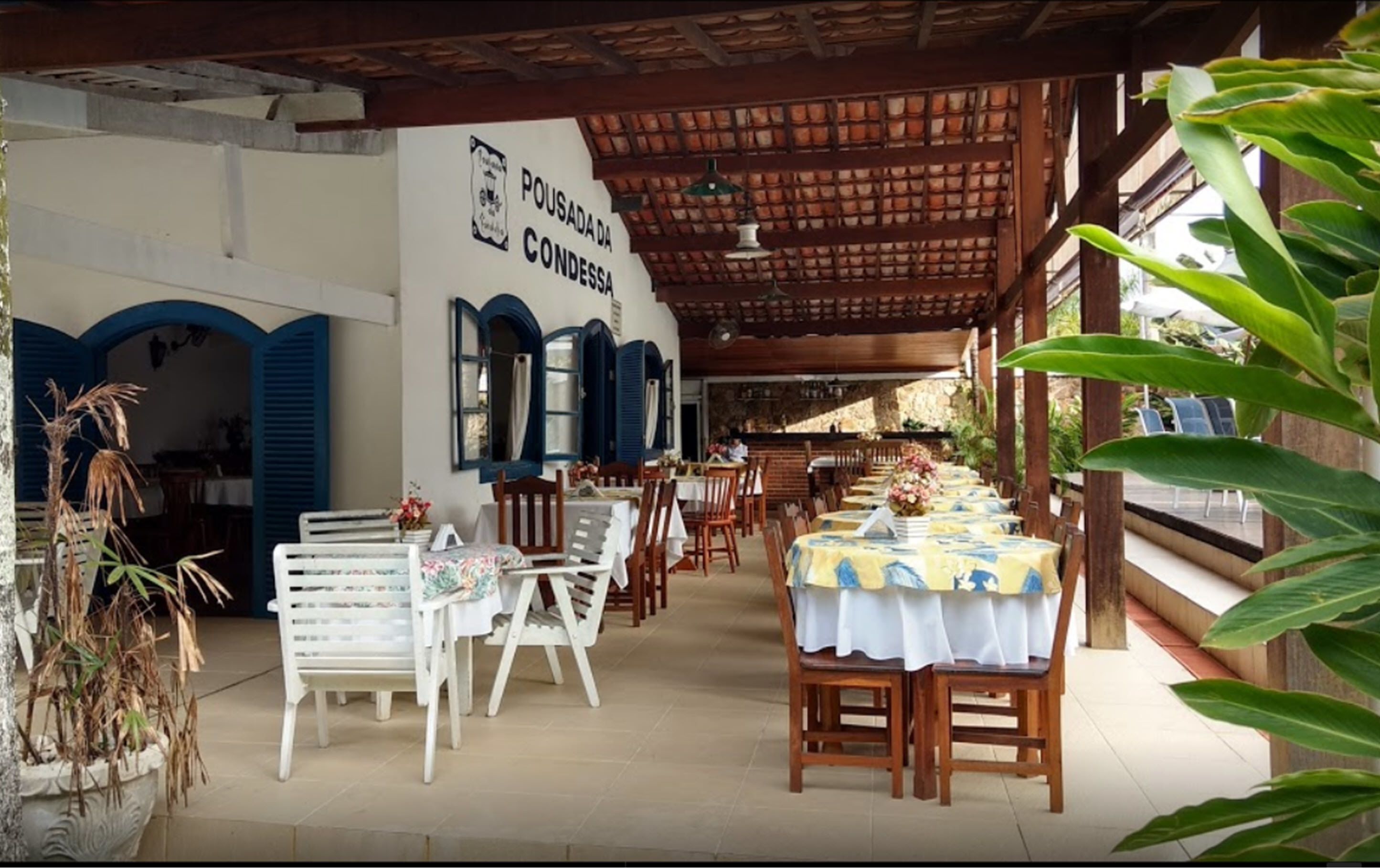 An outdoor restaurant with tables and chairs, a covered area with a sign reading "POUSADA CONDESSA", and potted plants.