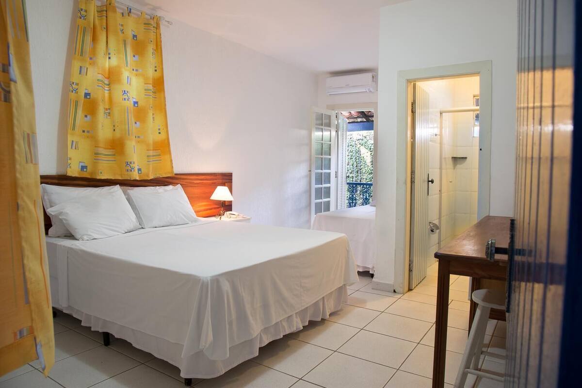 Habitación de hotel con cama, mesita de noche, lámpara y vistas al exterior a través de una ventana.