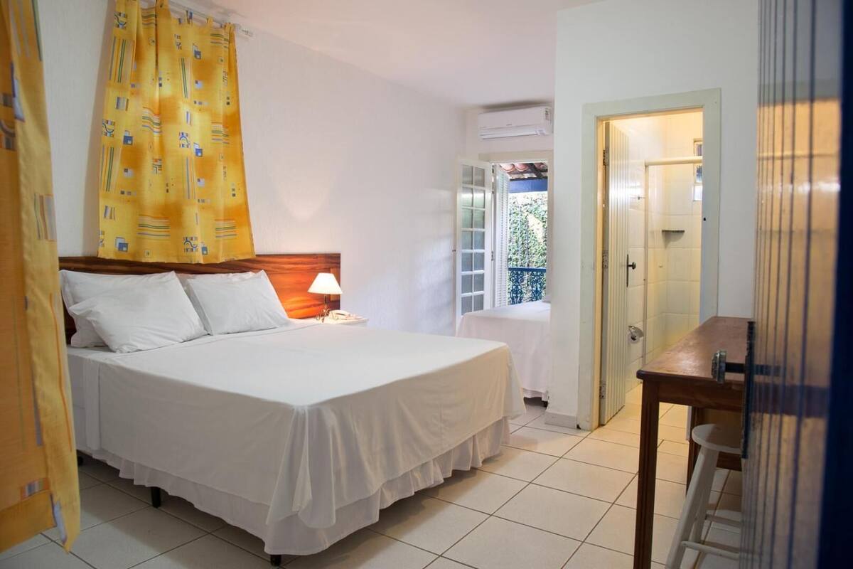 Une chambre d’hôtel avec un lit, une table de chevet, une lampe et une fenêtre donnant sur un paysage verdoyant.