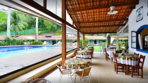 A covered outdoor dining area with tables and chairs, overlooking a swimming pool and lush greenery. - Pousada Da Condessa (Paraty)