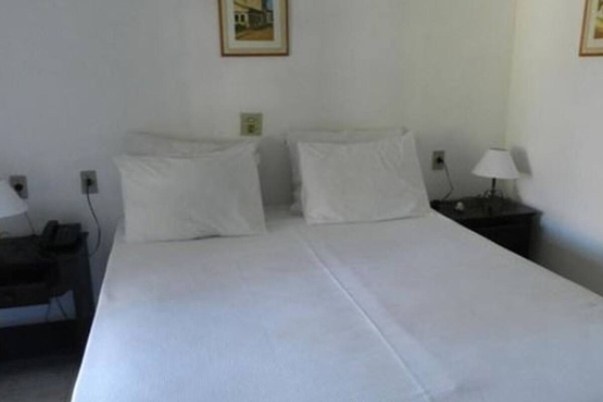 Une chambre simple et épurée, avec un lit simple, une table de chevet avec une lampe et un téléphone fixé au mur.