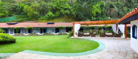 A courtyard with a paved walkway, outdoor seating, and a view of a forested hillside.