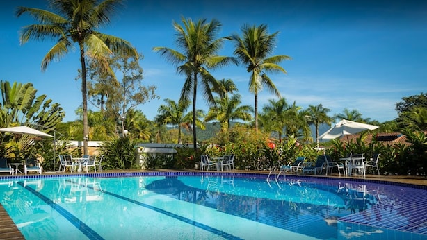 A swimming pool with clear blue water, surrounded by palm trees and lounge chairs. - Pousada Da Condessa (Paraty)