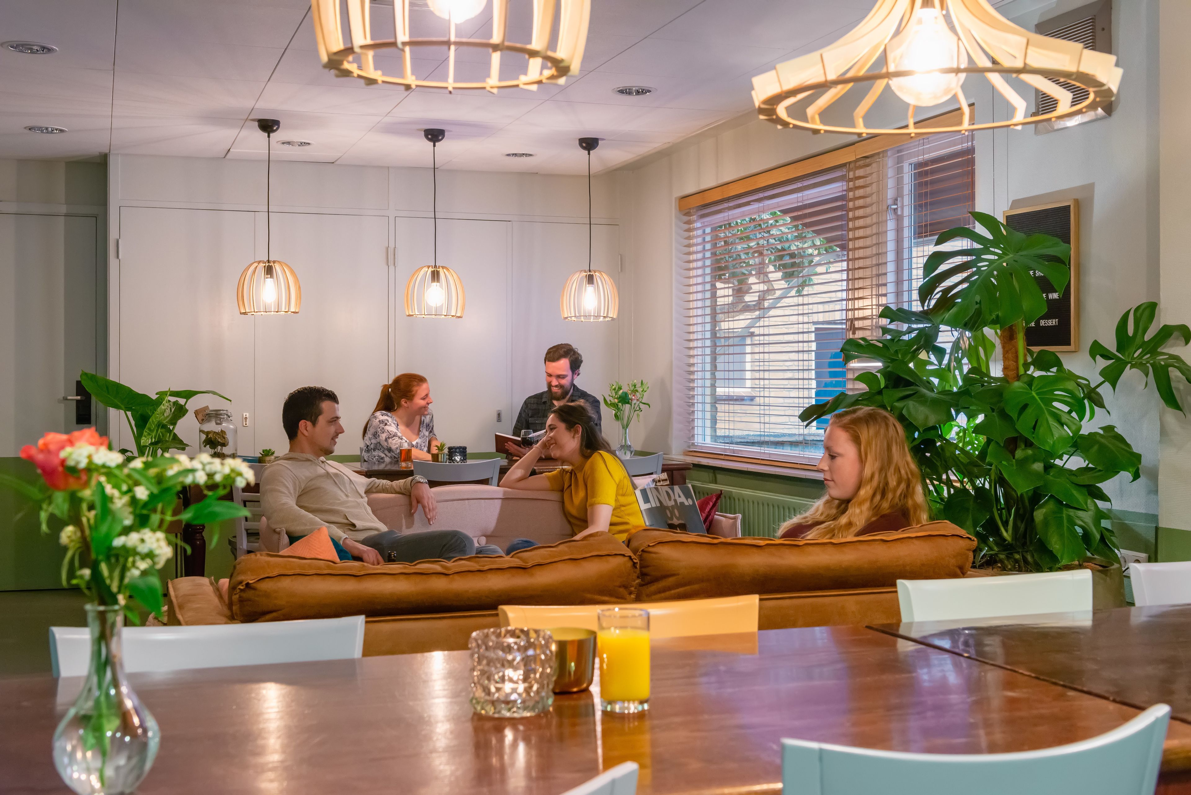 A modern lounge area with leather sofas, pendant lighting, and a dining table with a glass of orange juice.