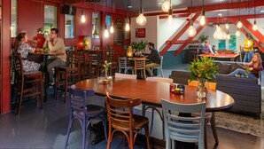 A modern dining area with wooden tables and chairs, hanging light fixtures, and a red accent wall. - Stayokay Arnhem - Hostel (Arnhem)