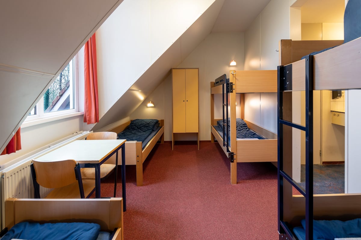 A dormitory room with bunk beds, a desk, and a chair.