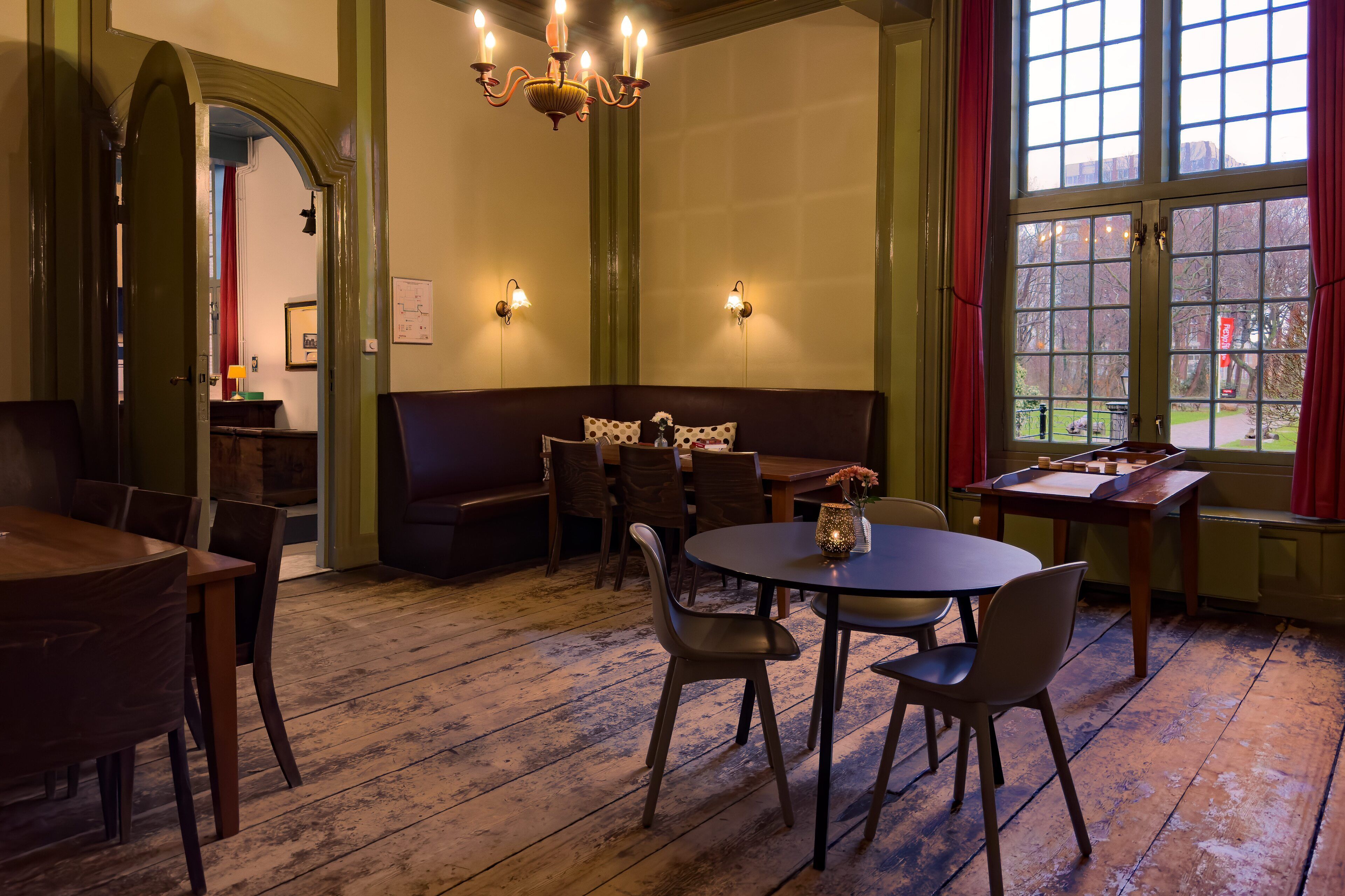 A cozy room with a wooden floor, a round table, and a bench. There are wall sconces and a chandelier.