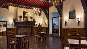 Un restaurante con mesas y sillas de madera, una chimenea de ladrillo y candelabros sujetos a la pared.