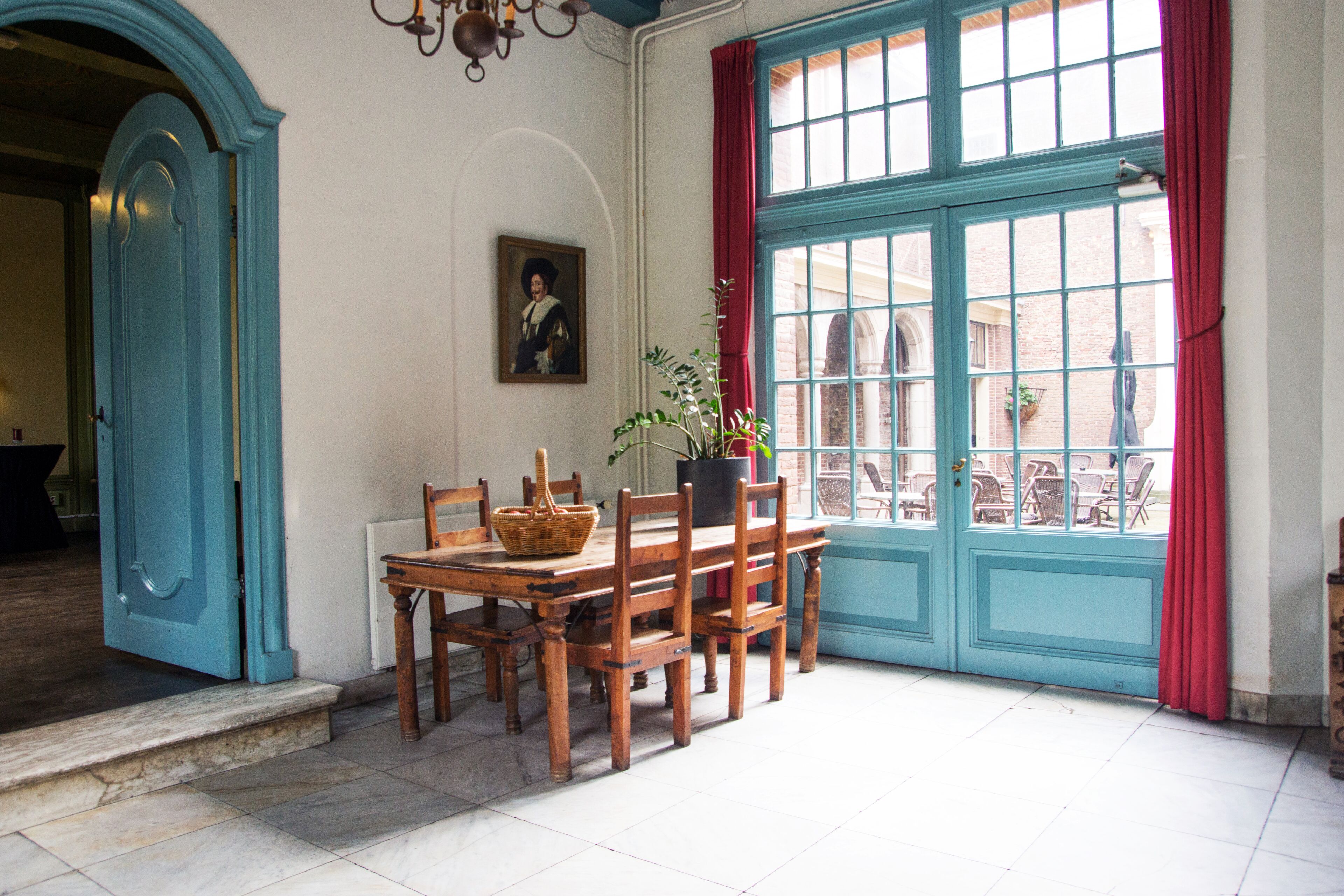 Un comedor con una mesa y sillas de madera, una planta en maceta y vistas por una puerta azul.