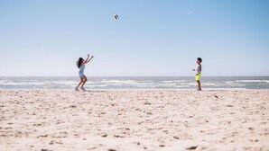 Dos personas jugando al voleibol en una playa arenosa, con el océano al fondo.