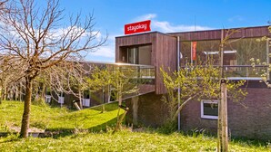 Un bâtiment moderne, orné d’une enseigne « stayokay », entouré d’arbres et d’herbe.