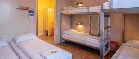 Ein Hotelzimmer mit Stockbetten, einem Einzelbett und einem kleinen roten Hocker.