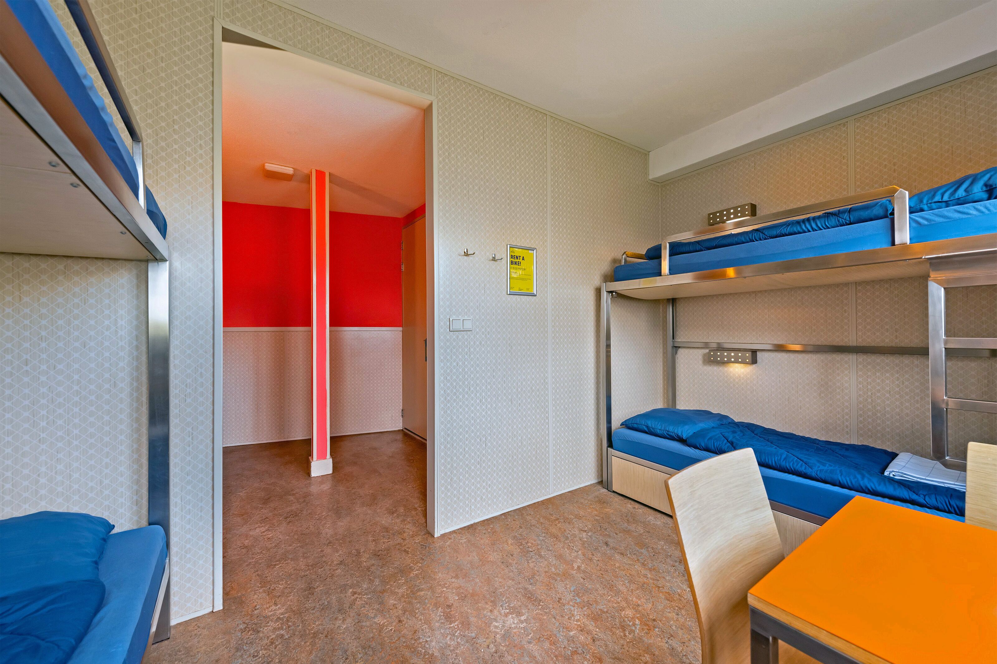 A compact hotel room with bunk beds, a small table, and a chair.
