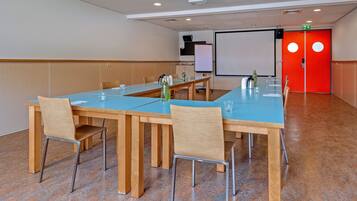 A conference room with a long table, chairs, a projector screen, and a red door.