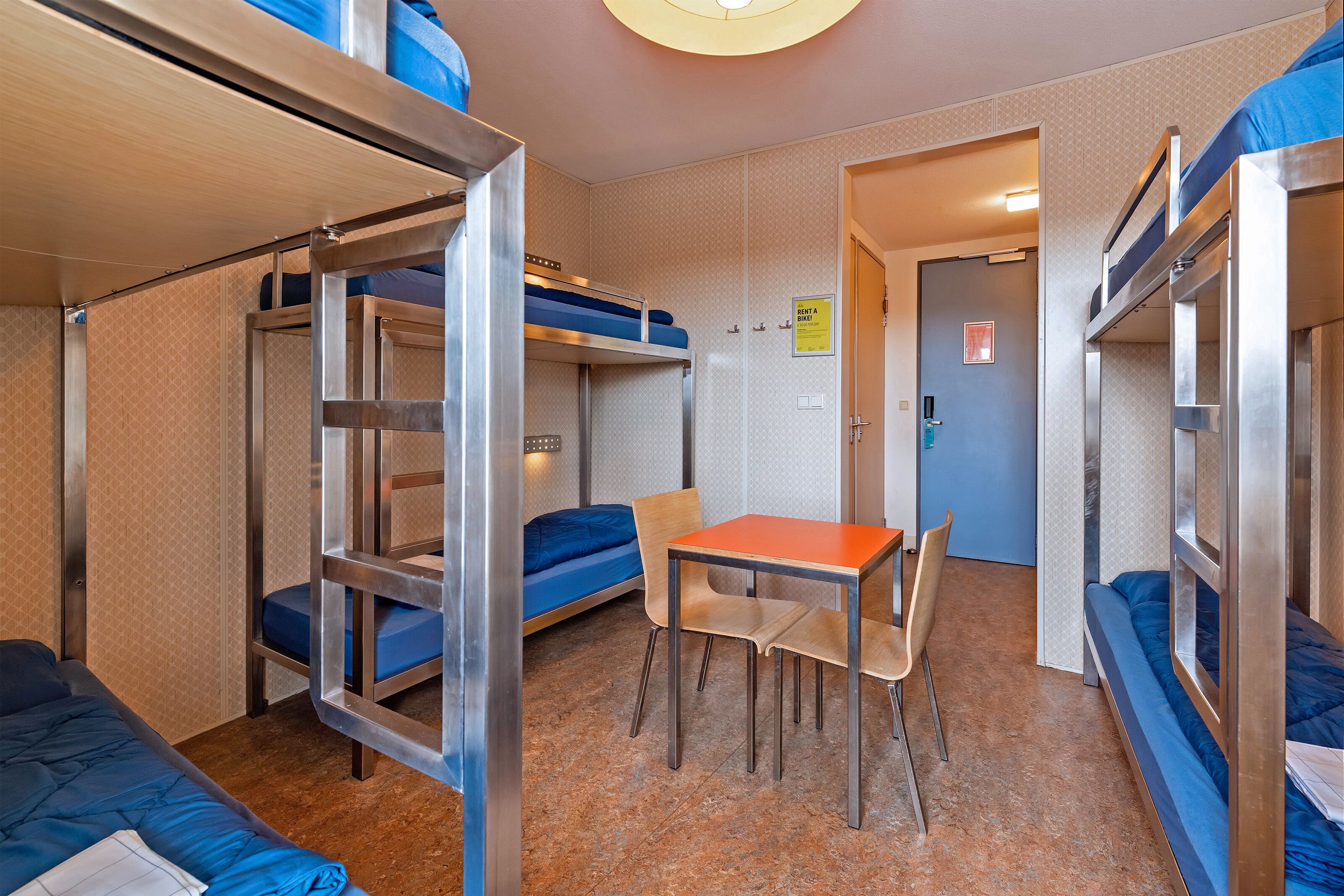 A dormitory room with bunk beds, a small table, and chairs.