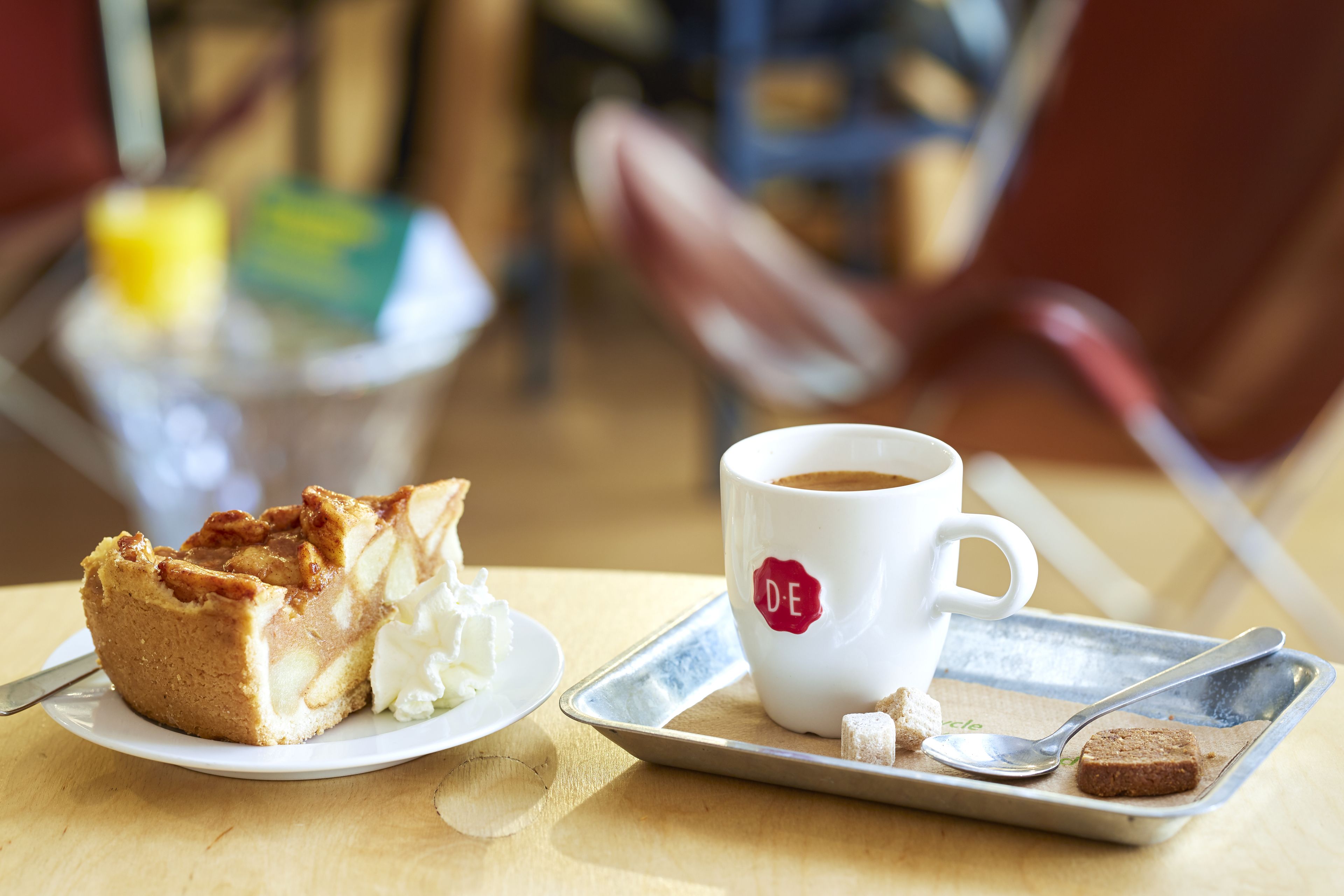 Una bandeja con una porción de pastel, una taza de café y una cuchara sobre una mesa.