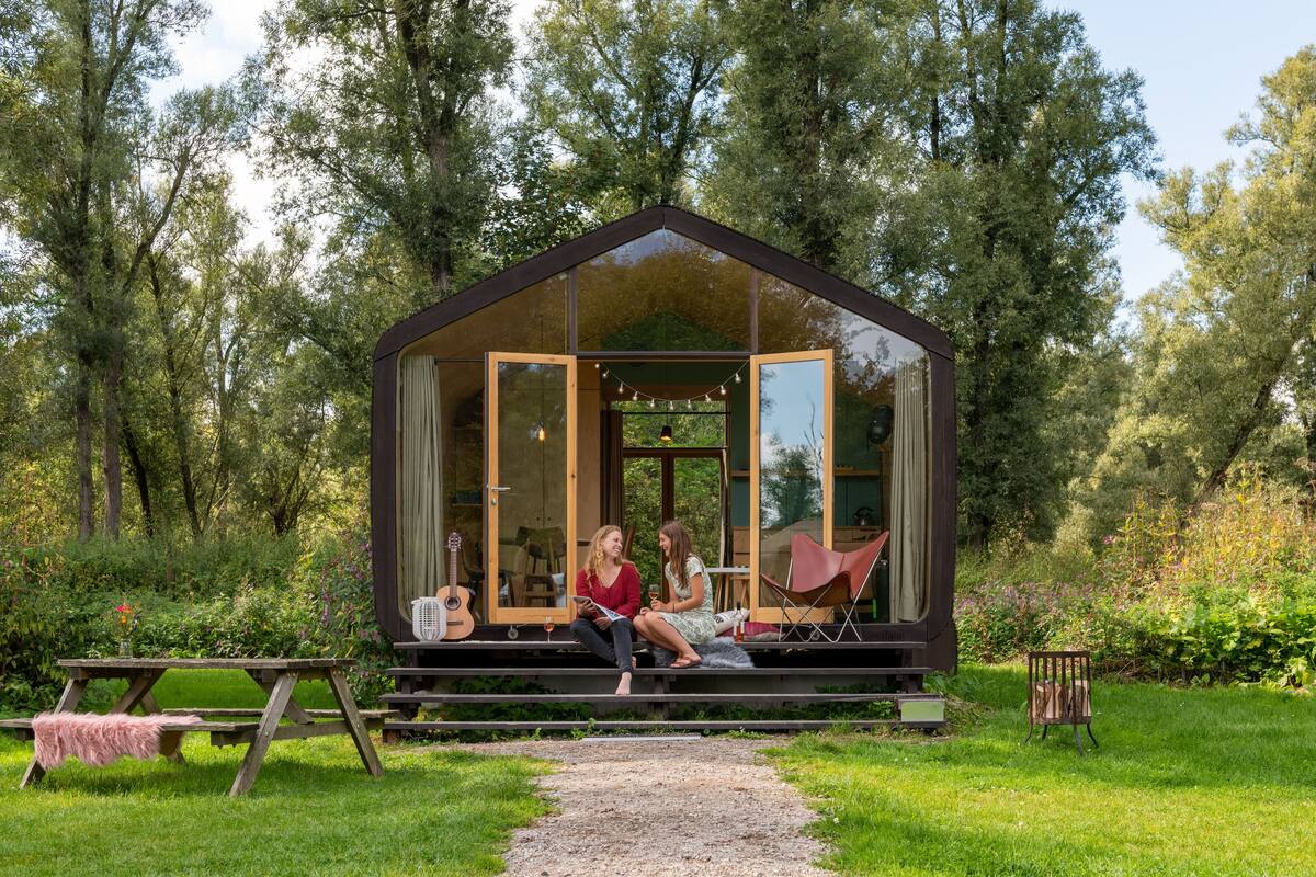 A glass-roofed cabin with a wooden deck, surrounded by lush greenery.