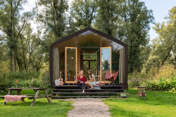 A glass-roofed cabin with a wooden deck, surrounded by lush greenery.