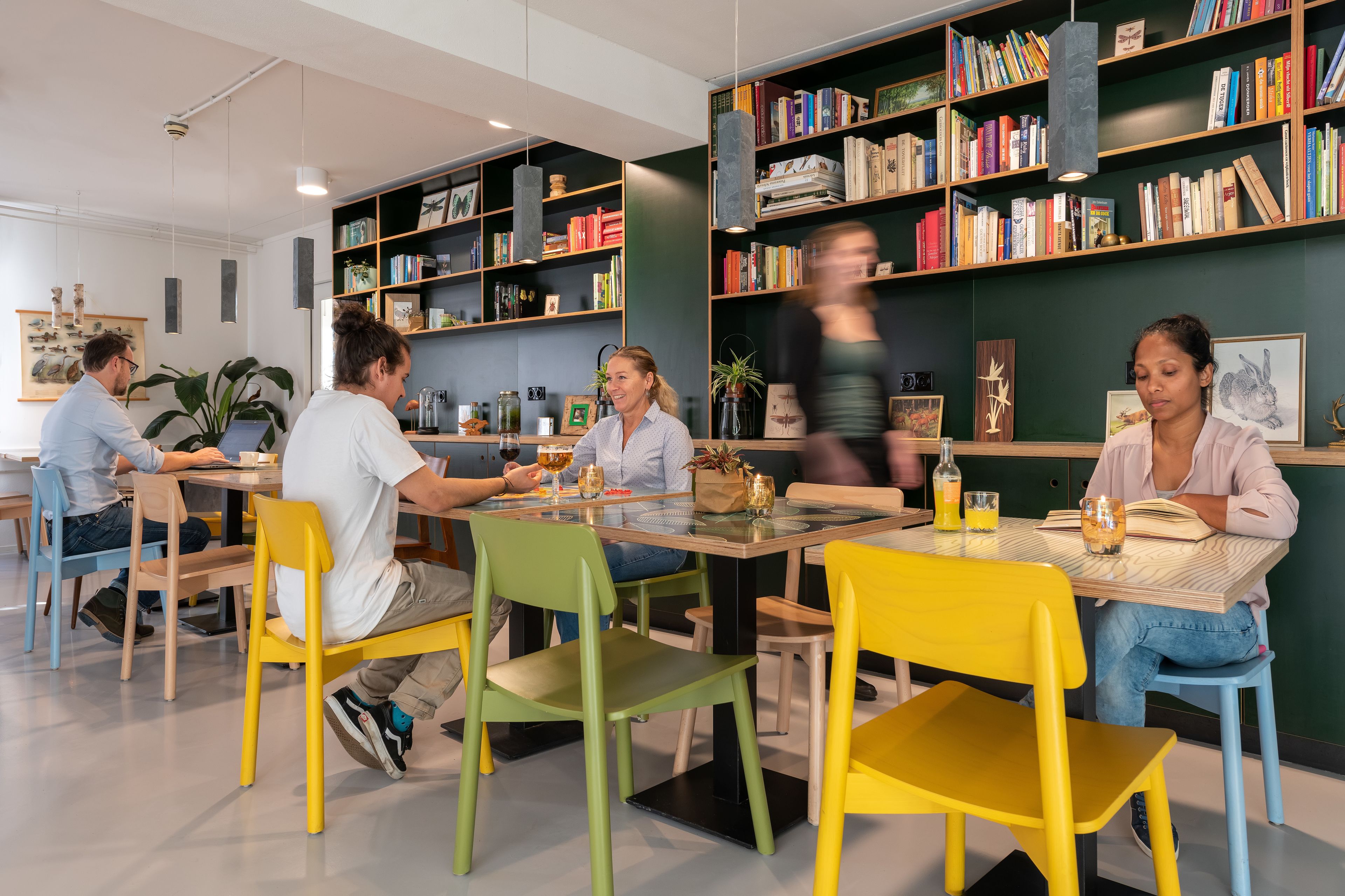A modern cafe with colorful chairs and tables, a bookshelf filled with books, and a relaxed atmosphere.