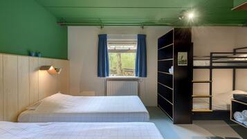 Quarto com duas camas, uma janela com cortinas, um radiador e uma cama beliche com prateleiras.