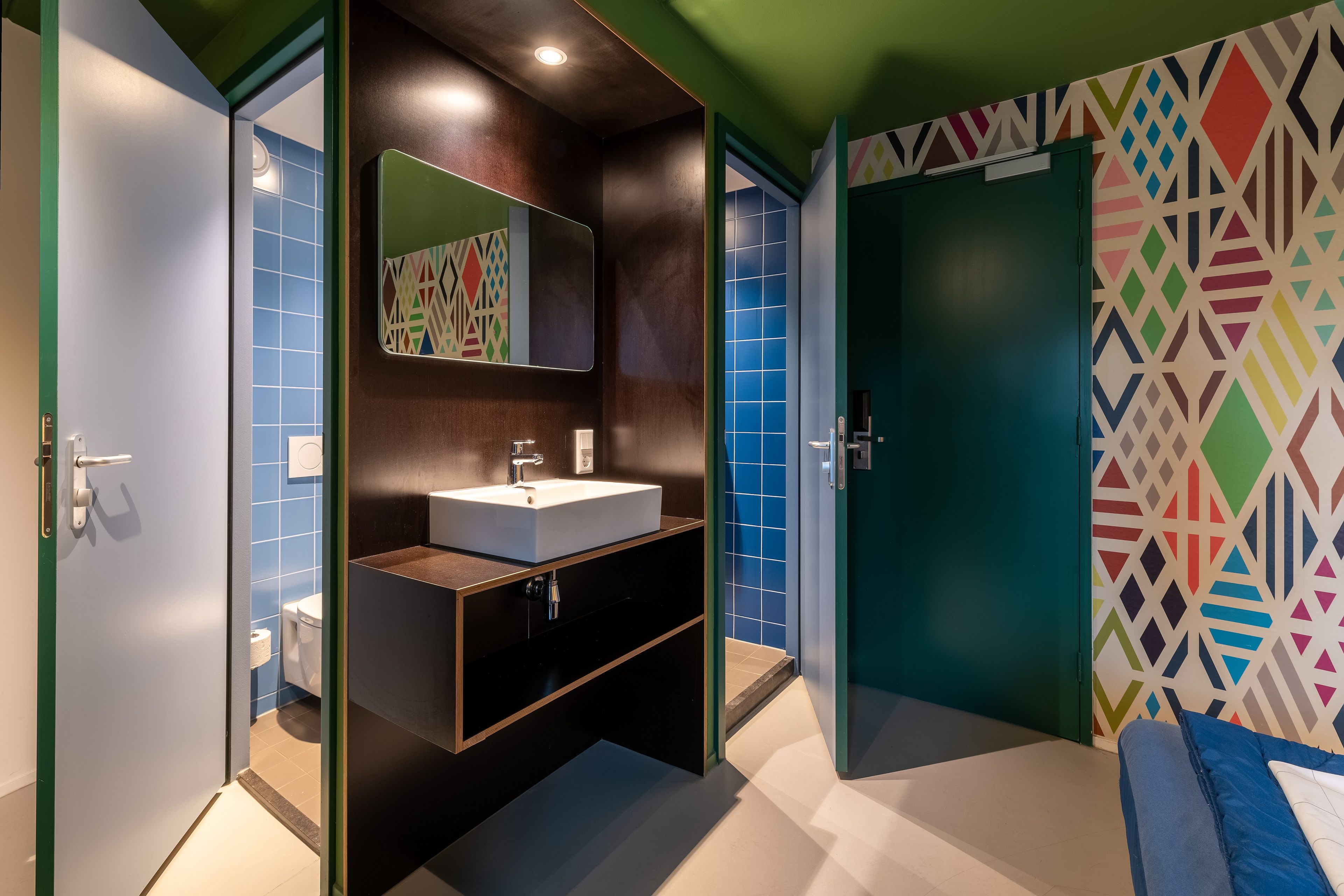 A modern bathroom with a large mirror, a white sink, and a patterned wall.