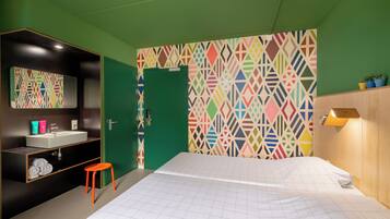 Un dormitorio con cama, una puerta verde, un baño con espejo y un patrón geométrico colorido en la pared.