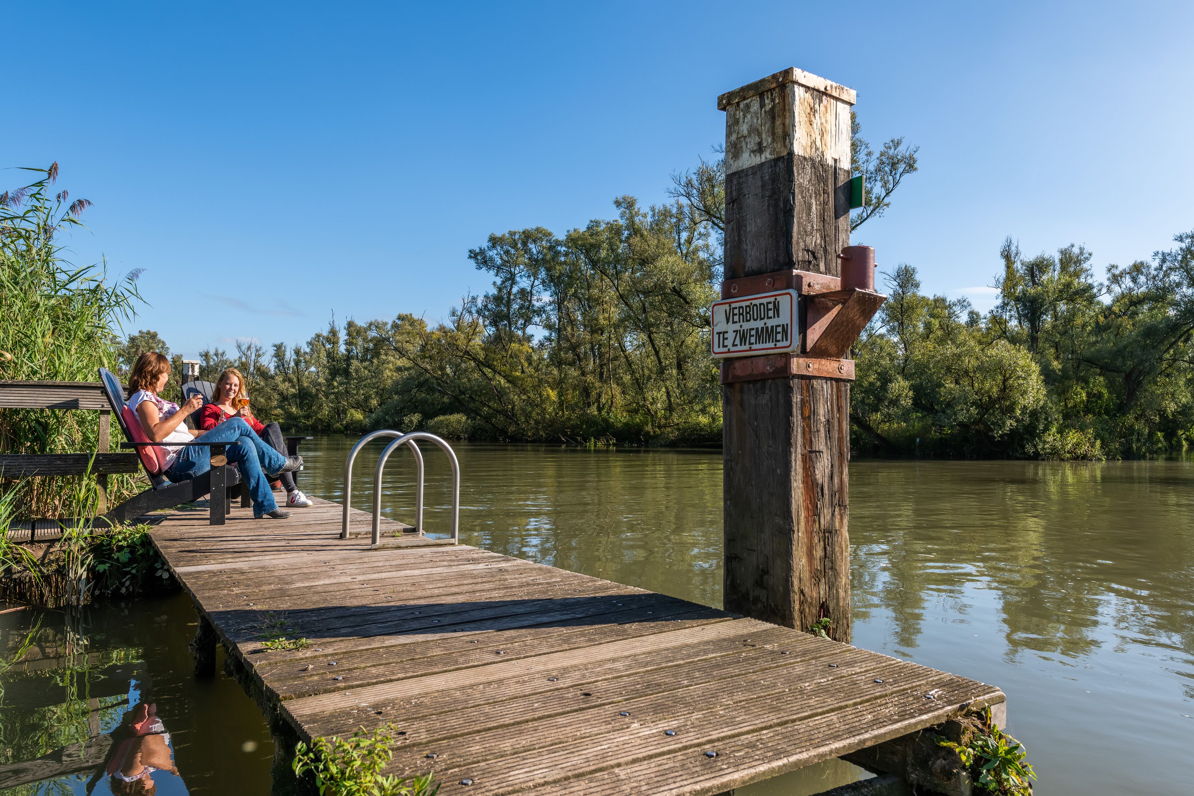 Un muelle de madera que se adentra en un río tranquilo, con un cartelón en el centro.