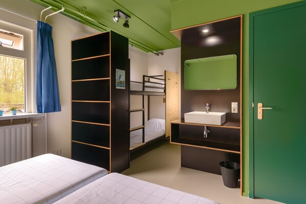 Una habitación pequeña con una cama litera, un lavamanos y una puerta verde.