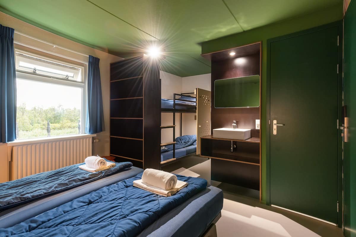 A room with two beds, a window with curtains, a bunk bed, a mirror, a sink, and a wardrobe.