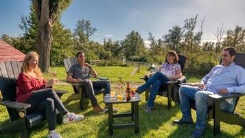 Four people sitting on outdoor furniture in a grassy area with a table between them, a bottle, and glasses on the table.