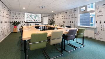 A conference room with a long table, green chairs, a projector screen, and a world map on the wall.
