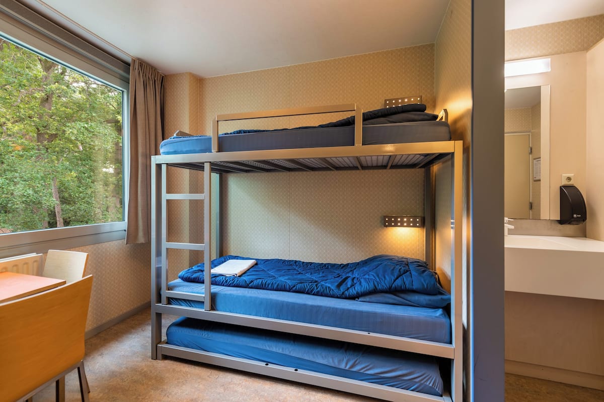 A bunk bed room with a desk and a window.