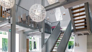 A spacious interior with a wooden staircase, high ceilings, and hanging spherical light fixtures. - Stayokay Soest - Hostel (Soest)