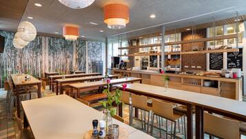 Un restaurante moderno con mesas y sillas altas, una zona de bar y una cocina visible a través de un panel de vidrio.