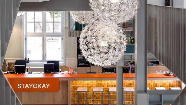 A modern interior with a central bar area, multiple hanging light fixtures, and a staircase. - Stayokay Soest - Hostel (Soest)
