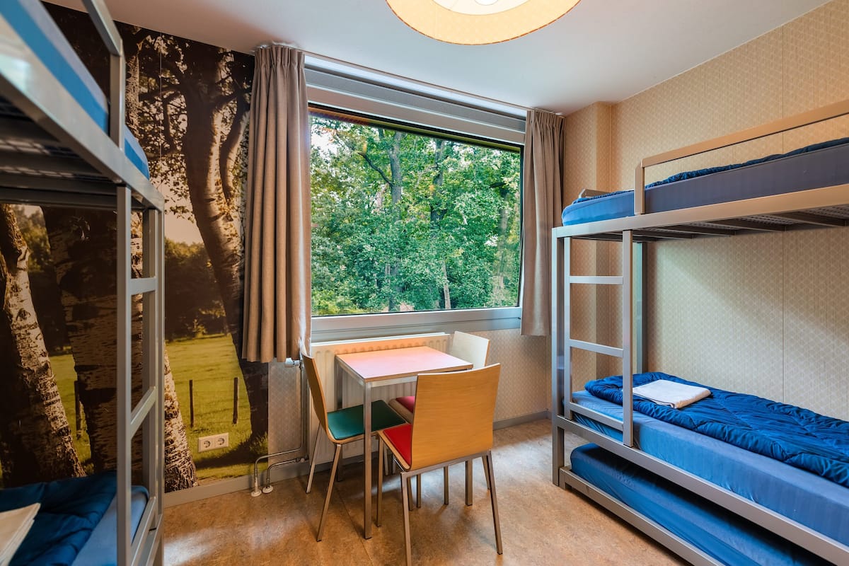 A room with bunk beds, a desk, and a chair. There is a window with a view of trees.