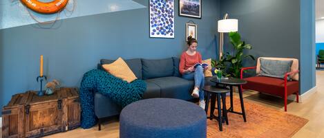 A modern living room with a blue wall, a wooden chest, a blue ottoman, a red chair, and a round table.