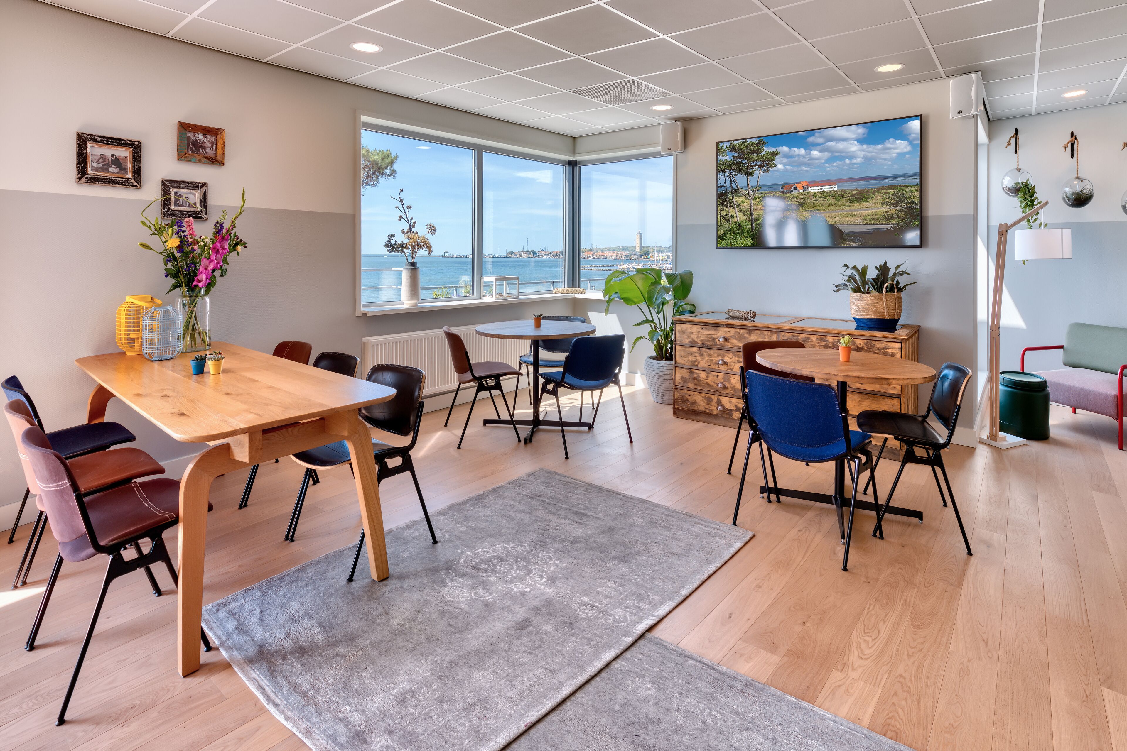 A modern dining area with a wooden table, chairs, and a view of the sea.